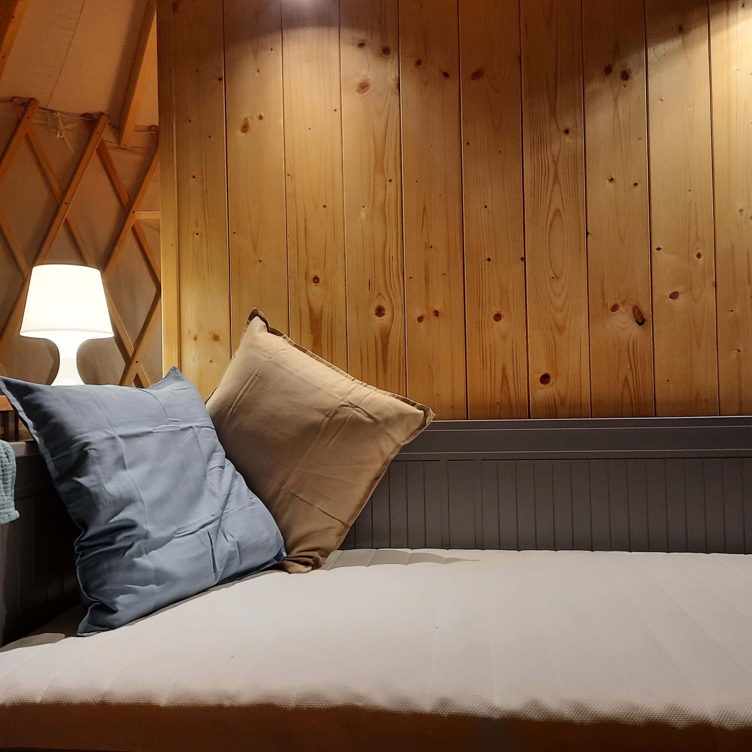 A bed with two pillows, a lamp, and wooden paneling on the wall.