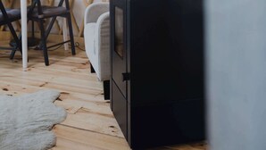 Una habitación con un estufa de leña negra, una mesa con sillas, una lámpara y una pared de celosía de madera.