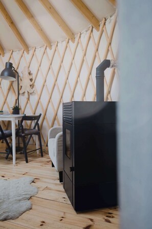 Una habitación con un estufa de leña negra, una mesa con sillas, una lámpara y una pared de celosía de madera.