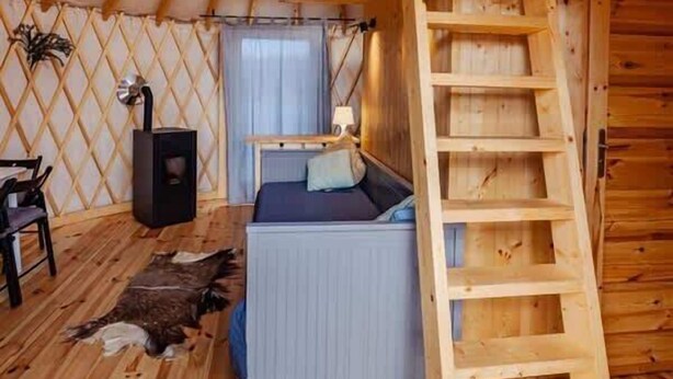 Una yurta con interior de madera, una cama, una escalera y un pequeño calentador.