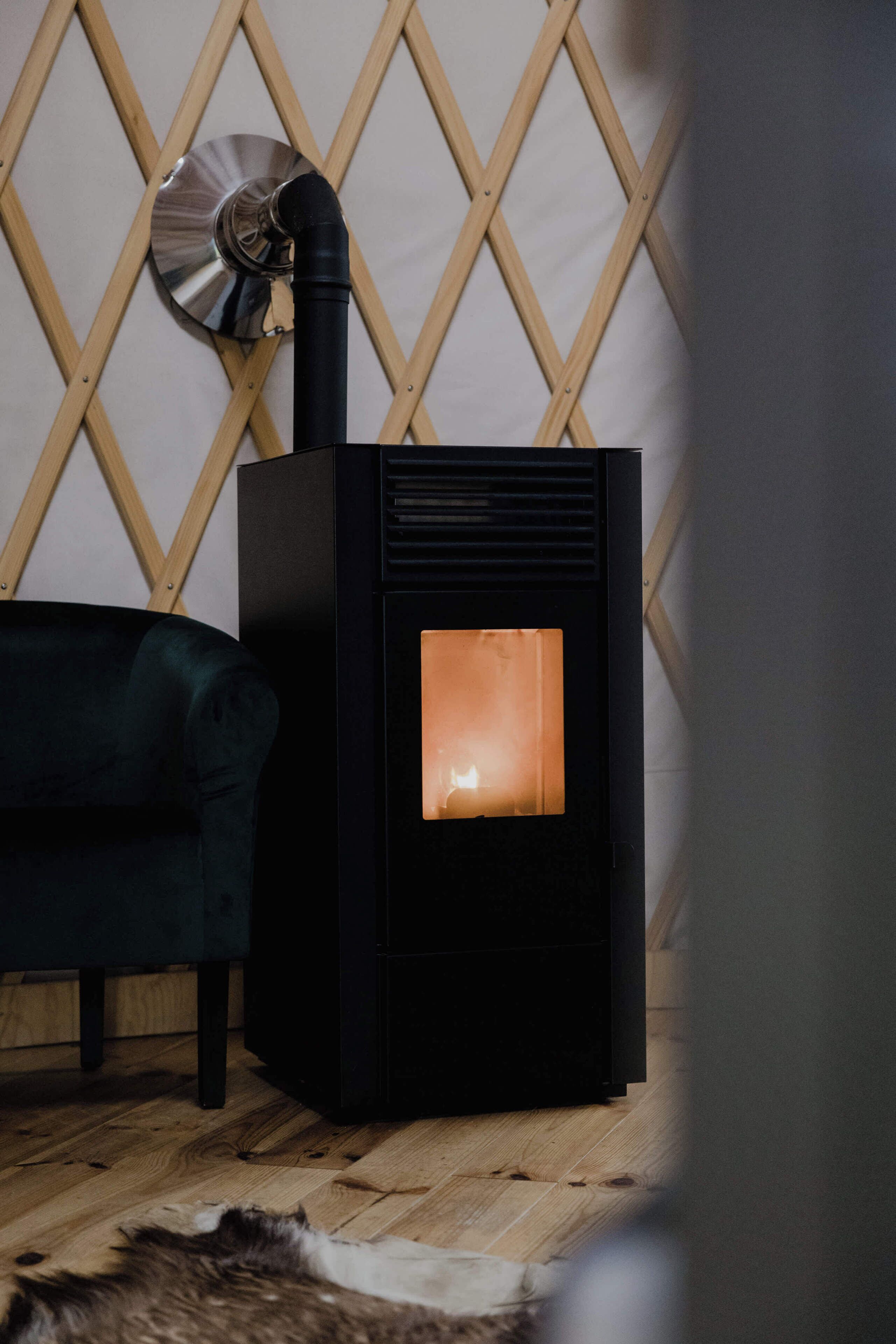 A room with a black wood-burning stove, a dark green sofa, and a wooden floor.