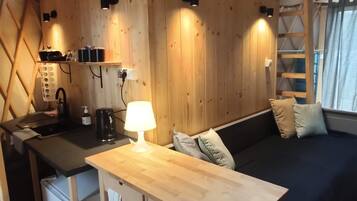 A compact wooden cabin with a kitchenette, a dining table, and a sofa.
