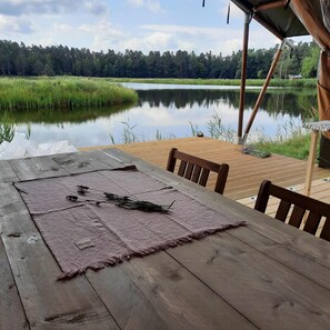 A wooden table with a placemat and a chair, overlooking a calm lake and forest.