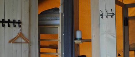 A room with a wooden door, a coat rack, a shelf with a cup, and a hanging bag.