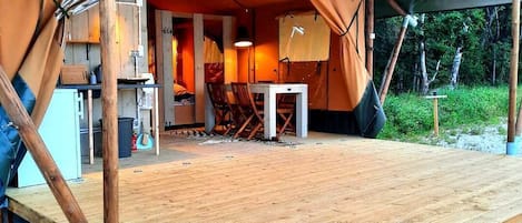 A tent with a wooden deck, a table, chairs, and a small kitchen area.