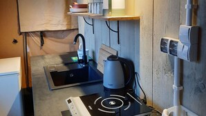 Una kitchenette compacta con un lavamanos, un hervidor, una estufa y una repisa con una lámpara.