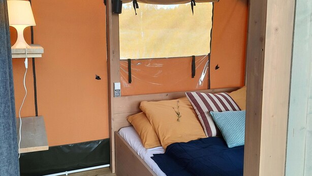 Una cama individual con cabecera de madera, una lámpara de noche y una ventana con cortina.
