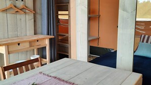 Una mesa de madera con un mantel rosa y una planta, un banco de madera y una cama con cubierta azul.