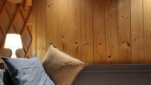 Una cama con dos almohadas, una lámpara y paneles de madera en la pared.