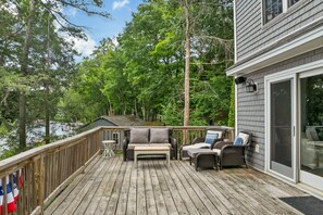 A wooden deck with outdoor furniture, a view of a lake, and a house with a sliding glass door. - NEW FOR 2027 Lake Winnipesaukee Waterfront Sleeps 12 (Moultonborough)