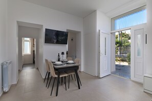 A modern dining area with a table set for four, a flat-screen TV mounted on the wall, and a door leading to an outdoor area. - Seaview and Terrace Apartment La Vita (Kostrena)