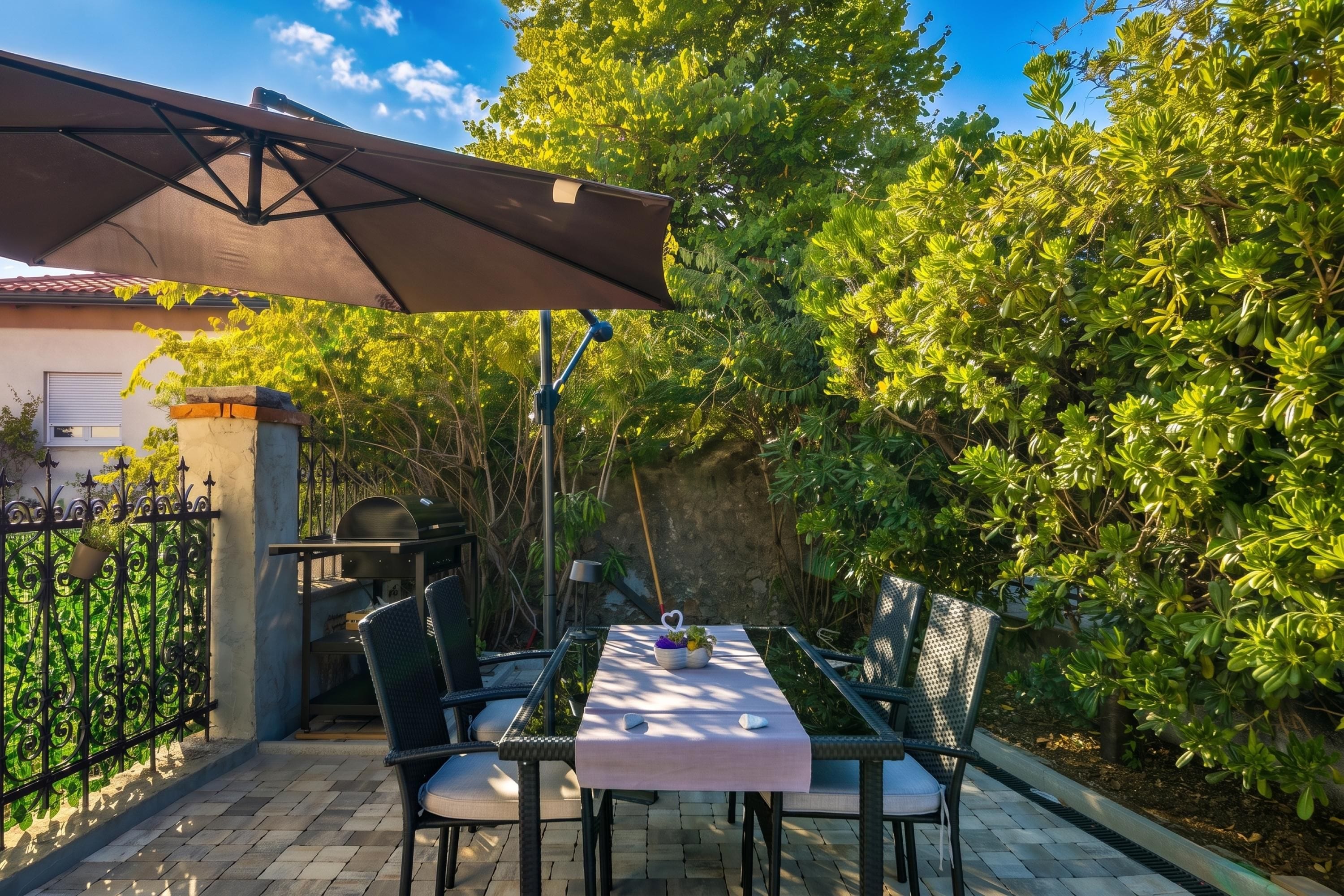 An outdoor patio with a table and chairs, a grill, and a covered area.