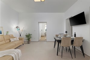 A modern living room with a sofa, a dining table with chairs, a flat-screen TV mounted on the wall, and a potted plant. - Seaview and Terrace Apartment La Vita (Kostrena)