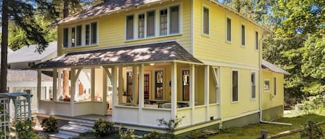 A two-story yellow house with a porch, a chimney, and a fenced yard.