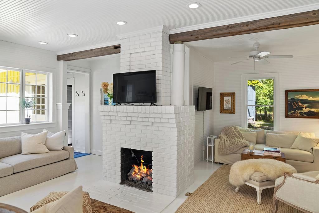 Una sala de estar con chimenea de ladrillo blanco, un televisor montado encima y un sofá.