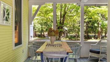 A covered porch with a table and chairs, surrounded by trees.