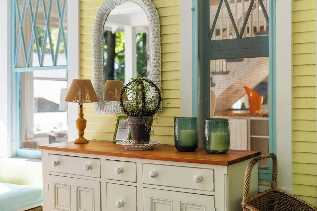 A white dresser with drawers, a mirror, a potted plant, and two green glass vases.