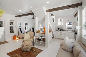 Een ruime woonkamer met een bank, een salontafel en een eettafel met stoelen. Er is een trap die naar een hoger gelegen verdieping leidt.