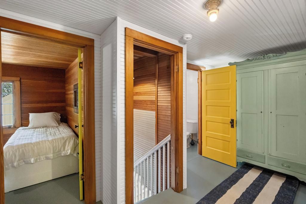 A bedroom with a bed, a wooden wardrobe, and a yellow door.