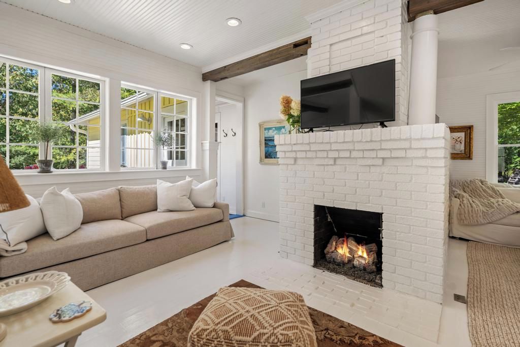 A living room with a white brick fireplace, a flat-screen TV mounted above it, and a beige sofa.