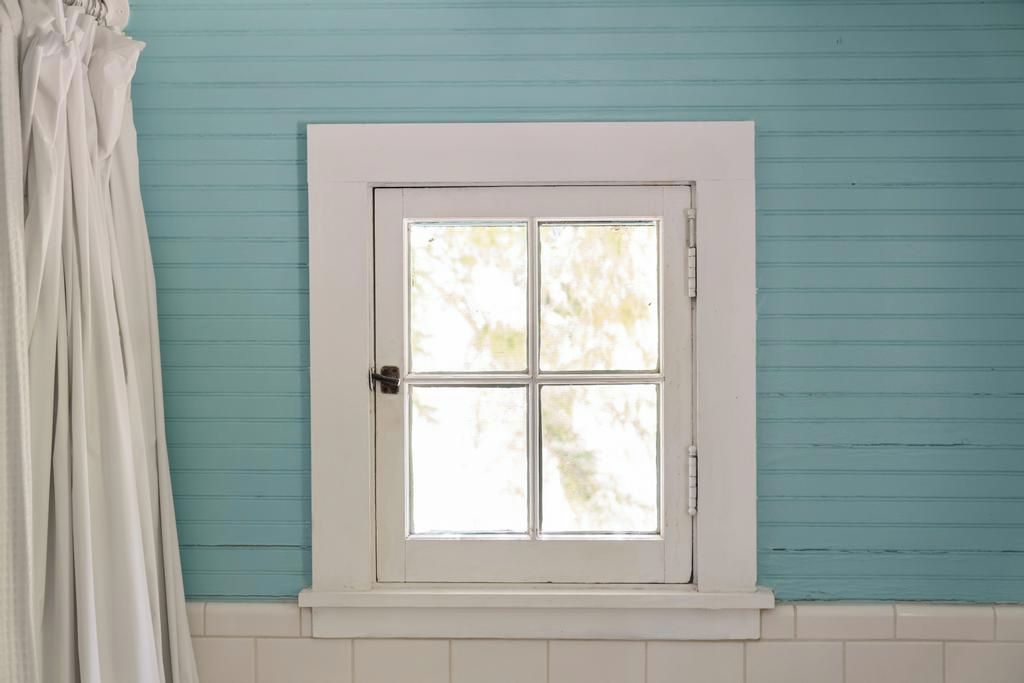 A room with a white-framed window, a white door, and a teal-colored wall.