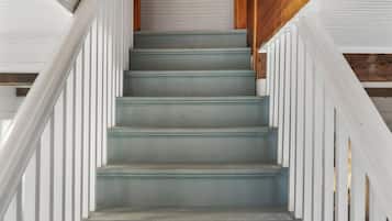 Un escalier avec des rampes blanches et une main courante en bois, menant à une porte fermée.