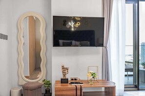 Ein modernes Wohnzimmer mit einem großen Spiegel, einem flachbildfernseher an der Wand, einem Couchtisch aus Holz mit dekorativen Gegenständen und Blick auf die Stadt durch große Fenster.