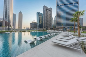 Una piscina en la azotea con sillones de descanso y un horizonte urbano al fondo.