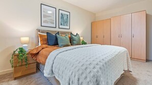 Ein Schlafzimmer mit einem Bett, Nachttischen, einem Kleiderschrank und zwei gerahmten Bildern an der Wand.