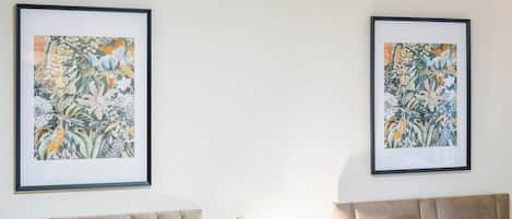 Une chambre d’hôtel avec deux lits, chacun doté d’une tête de lit, et deux œuvres d’art florales encadrées accrochées au mur.