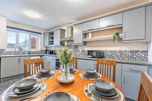 A modern kitchen with grey cabinets, a wooden dining table set for four, and a decorative vase. - #109 Modern 3-Bed Home in Moseley (Balsall Heath)