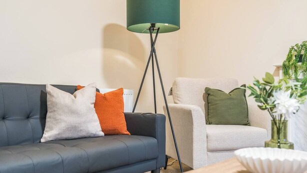 Ein modernes Wohnzimmer mit einem dunkelgrauen Sofa, einer Stehlampe, einem weißen Sessel und einem kleinen Tisch mit Blumen in einer Vase.