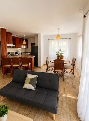 Ein Wohnzimmer mit einer Couch, einem Esstisch, Stühlen und einer Küchenzeile mit Schränken und Geräten.