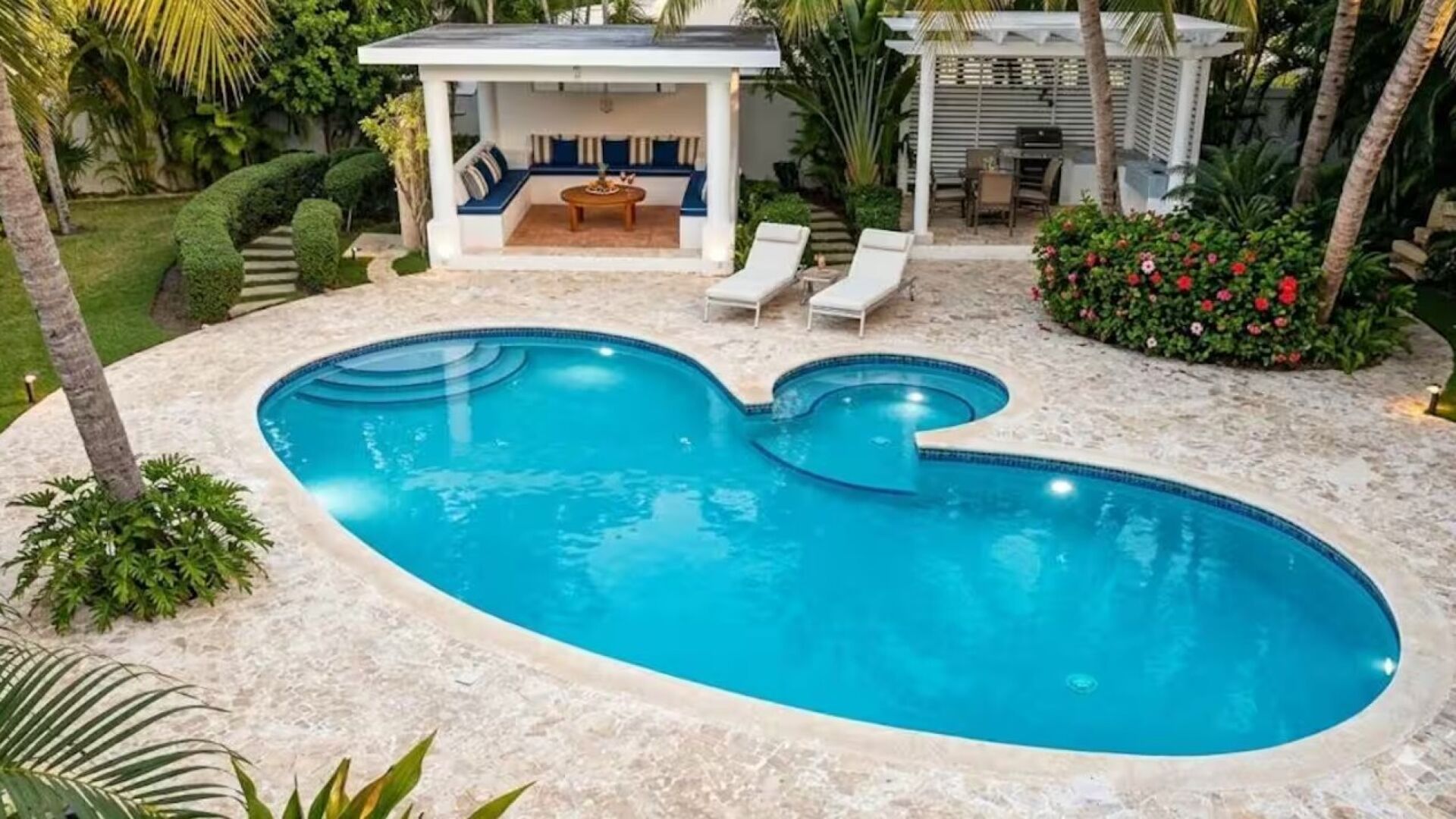 Une piscine dotée d’un espace salon aménagé en contrebas, entourée de palmiers et d’un jardin bien entretenu.