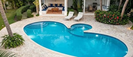 Piscina com área de estar embutida, rodeada por palmeiras e um jardim bem cuidado.