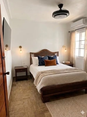 Ein Schlafzimmer mit einem Bett, Nachttischen, einem Deckenventilator und einem Fenster mit Vorhängen.