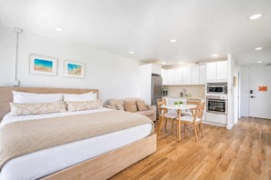 A bedroom with a large bed, a bedside table, and a small kitchenette with a microwave and oven. - Just Renovated Marine Surf Corner Unit with Free Parking! (Honolulu)