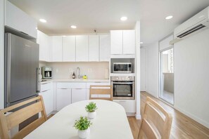 A modern kitchen with white cabinets, a built-in oven, a microwave, and a refrigerator. There is a dining table with chairs and two potted plants. - Just Renovated Marine Surf Corner Unit with Free Parking! (Honolulu)