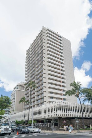 A tall, modern hotel with multiple floors and balconies, located near a street with cars and palm trees. - Just Renovated Marine Surf Corner Unit with Free Parking! (Honolulu)
