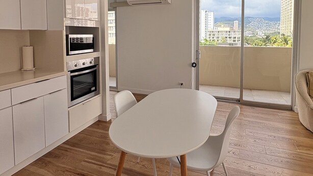 A modern kitchen with white cabinets, a built-in oven, and a dining area with a white table and chairs. - Just Renovated Marine Surf Corner Unit with Free Parking! (Honolulu)