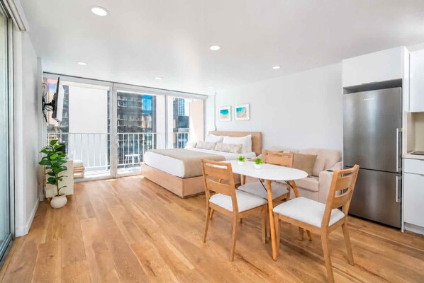 A modern apartment with a balcony, a dining area, a kitchen, and a large bed. - Just Renovated Marine Surf Corner Unit with Free Parking! (Honolulu)