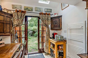 A cozy kitchen with wooden cabinets, a coffee machine, and a view of the garden through the open door. - Host Stay The 1890 Petersfield Retreat (Cambridge)