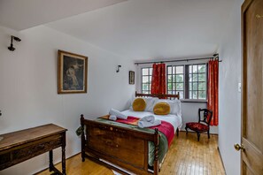 A bedroom with a wooden bed, a desk, a window with red curtains, and a painting on the wall. - Host Stay The 1890 Petersfield Retreat (Cambridge)