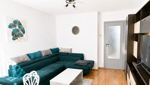 A modern living room with a sectional sofa, a dining table with chairs, a flat-screen TV, and a ceiling fan. - Bright & Cosy Apartment with Sunset View in Bucharest (București)