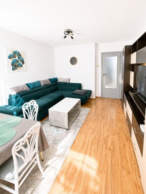 A modern living room with a sectional sofa, a dining table with chairs, a flat-screen TV, and a ceiling fan. - Bright & Cosy Apartment with Sunset View in Bucharest (București)