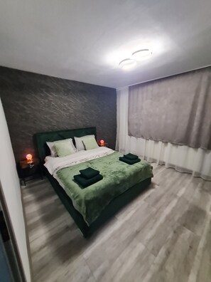 Ein Schlafzimmer mit einem Bett, Nachttischlampen, einem Fenster mit Vorhängen und einer Wand mit einer strukturierten Oberfläche.
