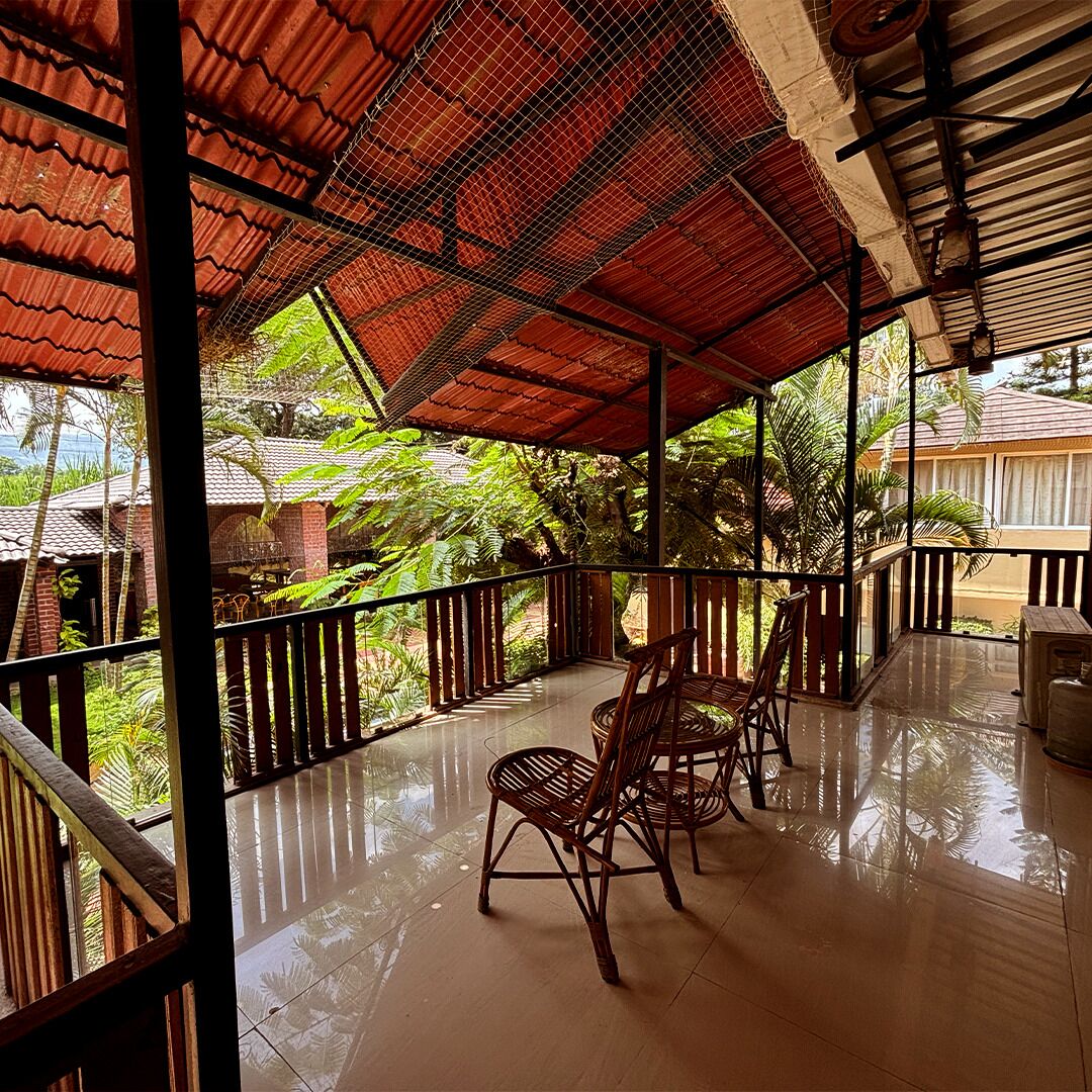 A covered outdoor area with a tiled floor, wooden chairs, and a view of surrounding greenery.