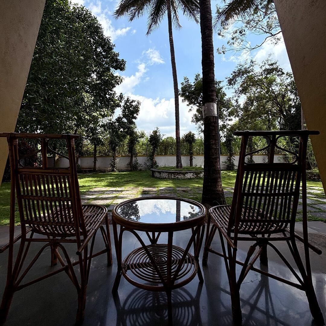 A glass-top table with two wicker chairs in an outdoor setting with trees and a clear sky.