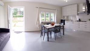 A modern kitchen with white cabinets, a dining table with chairs, and a view of the outdoors through large windows. - Bright apartment in a villa with a private garden, just a few minutes from Lucca (Marlia Capannori)