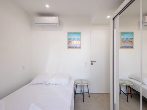 A bedroom with a bed, a small stool, a door, and a wall-mounted air conditioner. - (106) A la Joie de vivre 1 (Cannes)